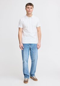 Hvit kortermet bomullspolo skjorte, kombinert med lyseblå jeans og brune sneakers med hvite snøringer. Rent, uformelt utseende.
