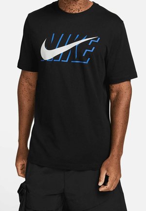 Persoon in een zwart Nike T-shirt met een blauw omlijnd "NIKE"-logo en het witte Nike-swooshlogo op de voorkant, gecombineerd met zwarte shorts.