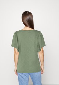 Oliven grøn kortærmet t-shirt med afslappet pasform, rund halsudskærmning og rynket skulderdetalje, lavet af letvægts, struktureret stof.