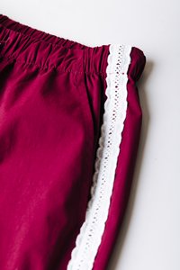 Μπορντό σορτς με ελαστική μέση, διακοσμημένα με λευκή δαντέλα κατά μήκος της πλευράς. Λείο ύφασμα με απαλή λάμψη και καθαρά ραφές.