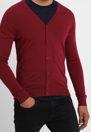 Cardigan bordeaux avec un col en V, des manches longues et des boutons à l'avant. Dispose de poignets et d'ourlet côtelés, superposé sur une chemise bleu marine. Texture de tissu lisse.