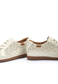 Zapatos de cuero beige con patrones florales cortados a láser, puntera redonda, cordones en la parte delantera y suela de goma marrón en contraste. Costura decorativa en los bordes.