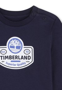 Granatowa bawełniana koszula z długim rękawem, z białym i niebieskim logo Timberland z grafiką drzewa, z guziczkami na ramieniu.