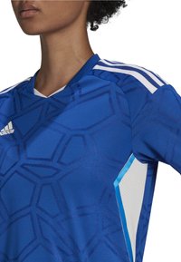 Maglia atletica blu con stampa geometrica, scollo a V, righe bianche a contrasto e tessuto testurizzato. Presenta un dettaglio in rete ai lati.