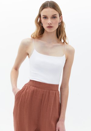 Camisola bianca con costine e sottili spalline, abbinata a pantaloni larghi in tessuto leggero e testurizzato di colore ruggine, con vita elastica.