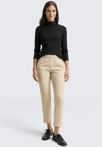 Zwart geribd coltrui-top met lange mouwen, gecombineerd met beige gestreepte cropped broek en zwarte veterlaarzen. Eenvoudige en veelzijdige outfit.
