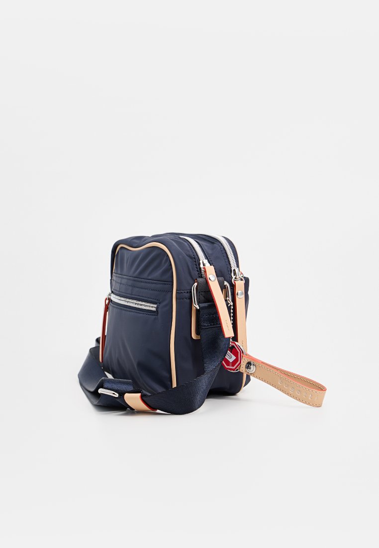 Sacoche en nylon marine avec des accents beige, dotée d'une poche zippée à l'avant, d'une sangle réglable et d'un porte-clés. Texture lisse et forme compacte.