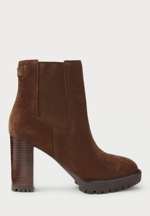 Stivale alla caviglia in suede marrone con pannelli elastici laterali, punta quadrata e tacco spesso in legno. Sola texturizzata per una buona aderenza.