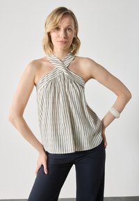 Top med halterneck med vertikale svarte og hvite striper, plissért design, krysslagt halslinje, kombinert med mørk marinebukser og et lyst armbånd.