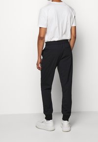 Czarne spodnie dresowe z elastycznym pasem, bocznymi kieszeniami i ściągaczami przy nogawkach, zestawione z prostą białą koszulką i białymi tenisówkami.