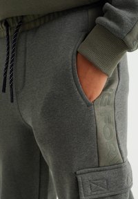 Grå joggers i mjukt tyg, med en sidficka och upphöjd textdetalj "FORWARD" i en mörkare nyans, samt elastisk midja.