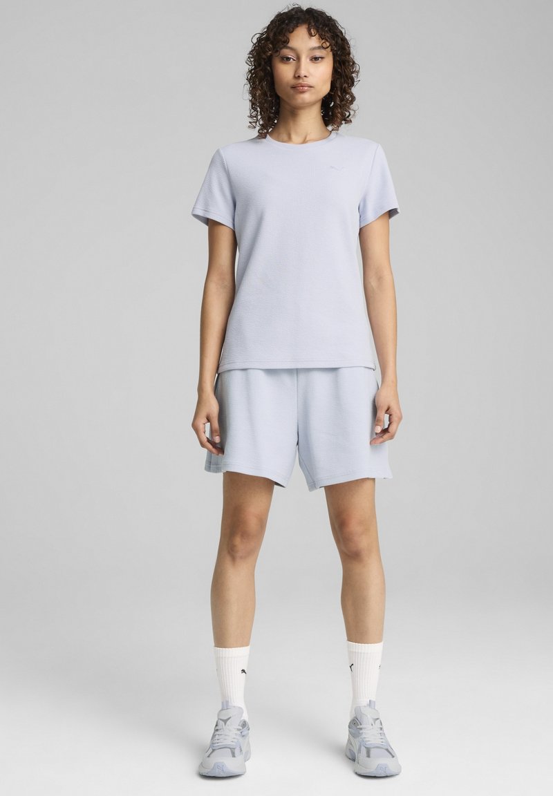 Lysblå kortærmet t-shirt og matchende shorts lavet af struktureret stof. Hvide sportsstrømper og grå sporty sko fuldender outfittet.