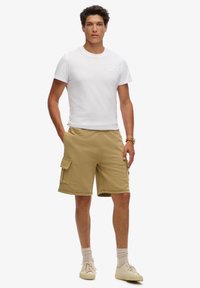 Pantalones cortos de cargo caqui con bolsillos laterales y un corte relajado, combinados con una camiseta blanca básica; modelo wearing calzado deportivo de color claro y calcetas.