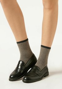 Schwarze Lederloafers mit glatter Oberfläche, kombiniert mit Socken im Fischgrätmuster in Beige und Schwarz, die einen gerippten Bund haben.
