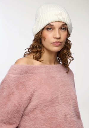 Berretto bianco a coste decorato con perline e un fiocco decorativo, abbinato a un maglione rosa pallido off-the-shoulder con una texture morbida.