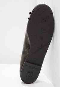Semelle d'une chaussure noire montrant des motifs embossés de chaussons de ballet et le nom de la marque PrettyBallerinas en lettres cursives.