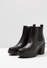 Musta nahkainen nilkkaboots, jossa on sileä pinta, pyöreä kärki, joustavat sivupaneelit ja paksu korko, jossa on teksturoitu pohja.