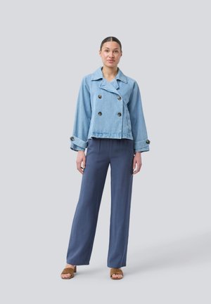 Light blue double-breasted denim jacket with large black buttons and wide sleeves, paired with navy flowy pants and brown sandals.