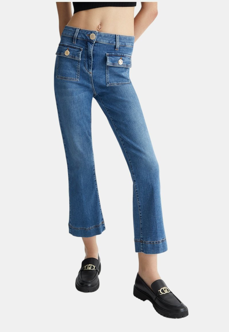 Jeans in denim con design a gamba corta e svasata in azzurro chiaro. Presentano due tasche frontali con bottoni dorati e cuciture a contrasto all'orlo.