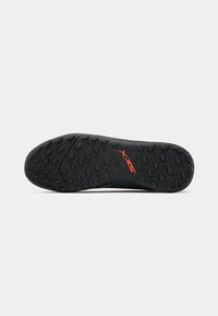 Black athletic shoe outsole with a textured pattern and orange branding, featuring circular and hexagonal grips for traction.