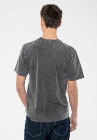 Gray short-sleeve t-shirt made of soft fabric. Features a relaxed fit and raw edge neck detail. Back view shows minimalistic design.