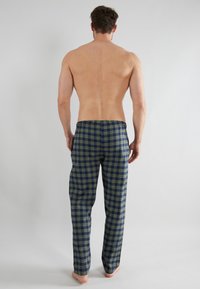 Pantalons de pyjama en coton à carreaux dans des tons de bleu marine et vert olive. Dotés d'une taille élastique et d'un design à jambes droites. Pieds nus visibles.