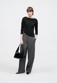 Μαύρο τοπ μακρυμάνικο με λαιμόκοψη σκάφος, γκρι πλισέ παντελόνια με φαρδιά μπατζάκια και λαμπερή μαύρη τσάντα με καμπυλωτή λαβή.