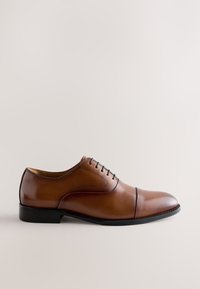Chaussure habillée Oxford en cuir marron avec semelle et lacets noirs, finition polie et détail bout droit sur fond neutre.