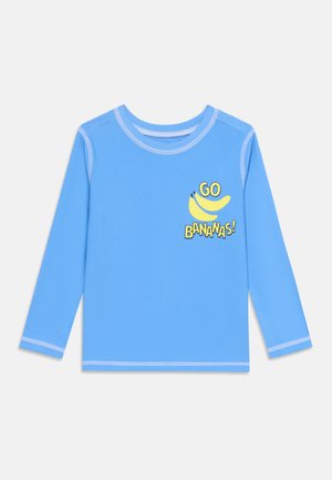 Hele sinine pikkade varrukatega särk valgete õmblustega ja kollase graafikaga, millel on kaks banaani ning tekst „GO BANANAS!“ rinnaosas.