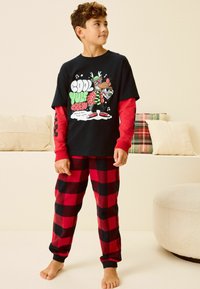 Czarny t-shirt z krótkim rękawem z grafiką przedstawiającą renifera, czerwone długie rękawy pod spodem, czerwono-czarną w kratkę piżamę.
