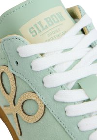 Zapatilla verde menta con un acabado texturizado, con cordones blancos, un acento de logo en marrón y una etiqueta crema que dice "SILBON SPORT FOOTWEAR."