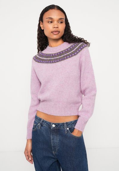 Gaiši violetas krāsu piegriezts džemperis ar adītu jaku, kam ir svītras un ģeometriski raksti. Apvienots ar augstiem zilo džinsu biksēm.