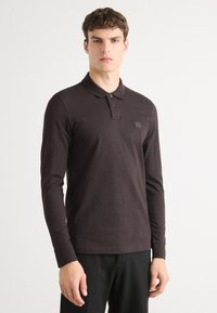 Mørkebrune poloer med lange ærmer i bomuld, der har en tre-knaps placket og et lille logo-patch på brystet.