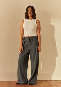 Top bianco a costine senza maniche abbinato a pantaloni grigi a vita alta e gamba larga. Tessuto liscio con pieghe sottili e una silhouette pulita.
