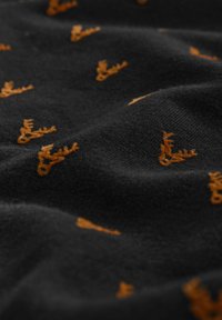 Il tessuto nero presenta un motivo ripetuto di piccoli palchi arancioni, con una texture morbida e una leggera caduta.
