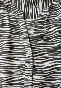 Blouse rayé noir et blanc avec un décolleté en V, dotée d'une patte de boutonnage et d'une texture de tissu lisse et léger.