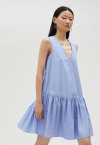 Light blue, sleeveless dress with a deep V-neck, pinstripes, and a ruffled hem. Features subtle embellishments throughout.