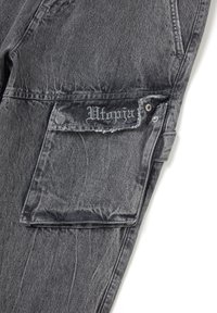 Pantalones cargo de mezclilla gris con una textura desgastada, gran bolsillo lateral y "Utopia" bordado en la solapa del bolsillo.