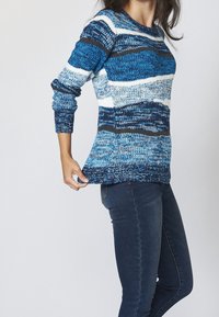 Stickad tröja med blå och vita horisontella ränder, rund halsringning och lång ärm. Elastisk struktur, kombinerad med mörk denimjeans.