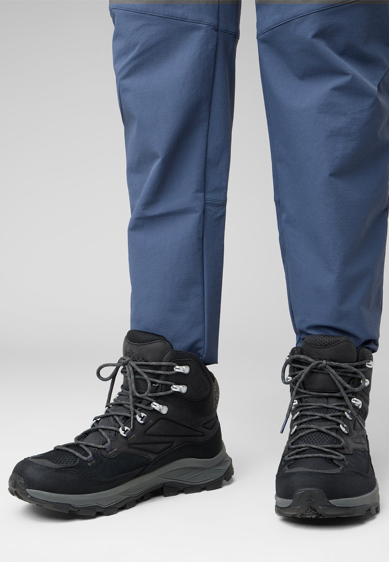 Schwarze Wanderstiefel mit grauen Akzenten, Schnürdesign, strukturiertes Mesh- und Gummi-Material, kombiniert mit blauen Hosen.