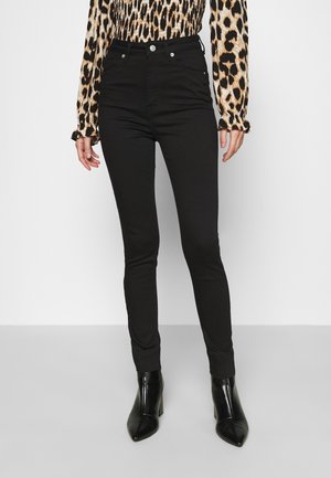 Femme portant un jean skinny taille haute noir, des bottines à talons noires et un chemisier à manches longues à imprimé léopard avec des poignets à volants.