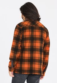 Orange og sort plaid flannelskjorte med lange ærmer, knapmanchetter, spidse kraver og en afslappet pasform. Struktureret stof.