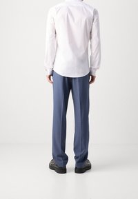 Wit shirt met lange mouwen en een afgeronde zoom, gecombineerd met lichtblauwe broek. Schoenen zijn zwart met een gladde textuur en dikke zolen.