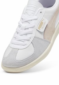 Białe sneakersy wykonane z skóry i zamszu, z szarymi i beżowymi akcentami, okrągłym noskiem, wiązanym designem oraz gumową podeszwą z teksturowanym dnem.