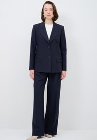 Marinblå skräddarsydd kostym med en dubbelknäppt kavaj med två knappar, slagkrage och vida byxor i ett slätt tyg.