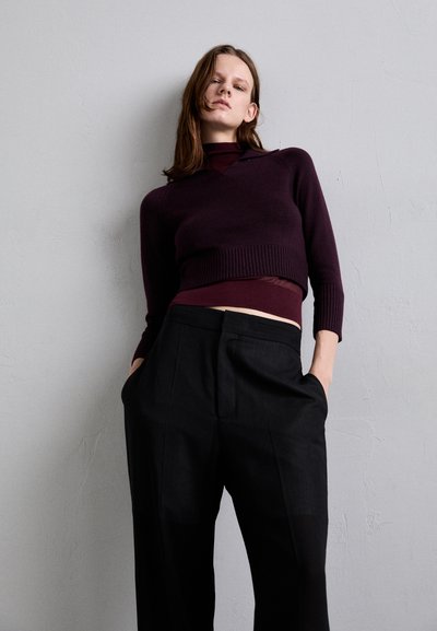 Sweater court violet avec ourlet côtelé sur un col roulé bordeaux, associé à un pantalon noir ample avec poches latérales.