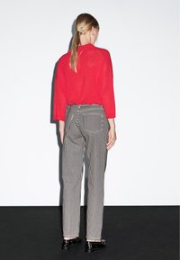 Maglione rosso lavorato a maglia, vestibilità rilassata, sopra pantaloni a righe bianche e nere con taglio dritto. Scarpe nere completano l'outfit.