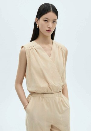 Beige mouwloze jumpsuit met een gewikkelde voorkant, elastische taille en zijzakken. Glad materiaal met een subtiele textuur, minimalistisch ontwerp.