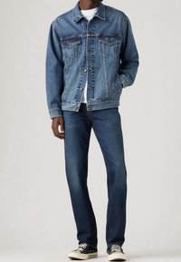 Jeansjacka i ljusblått med knappstängning och två bröstfickor, kombinerad med mörkblå jeans och svarta sneakers. Enkel, klassisk design.