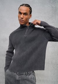 Grijze, geribbelde pullover met een hoge kraag en een halve ritssluiting. De stof is textuurachtig, met lange mouwen en een relaxte, boxy pasvorm.